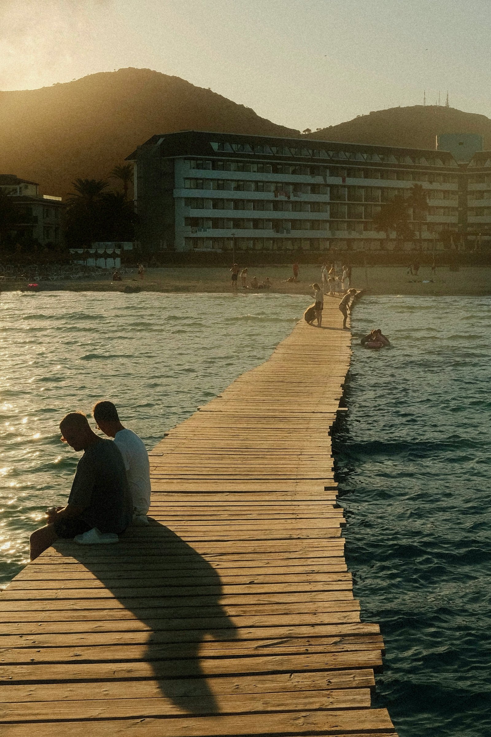 Two friends sitting together on a jetty at sunset