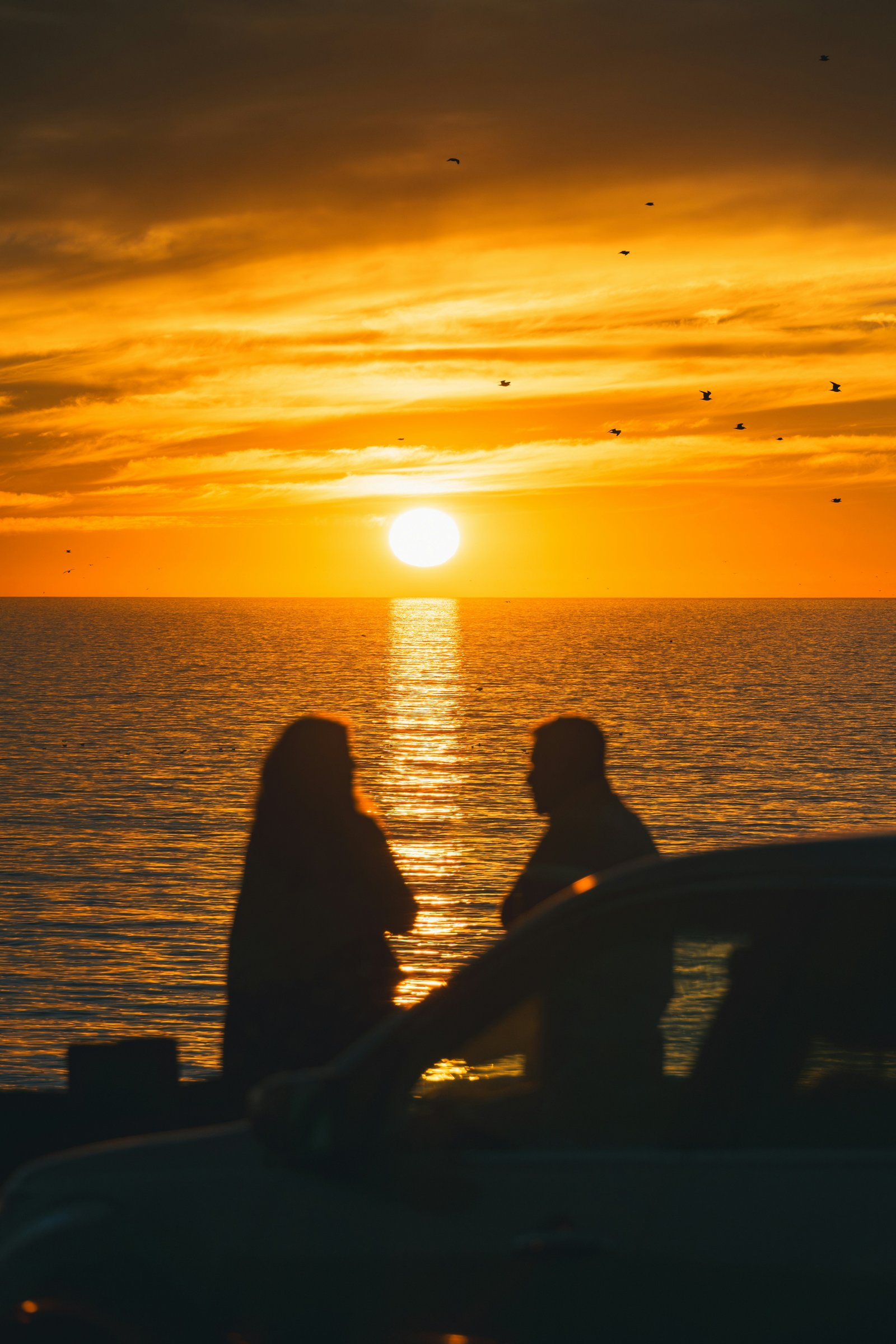 Two people watching the sun set over the sea
